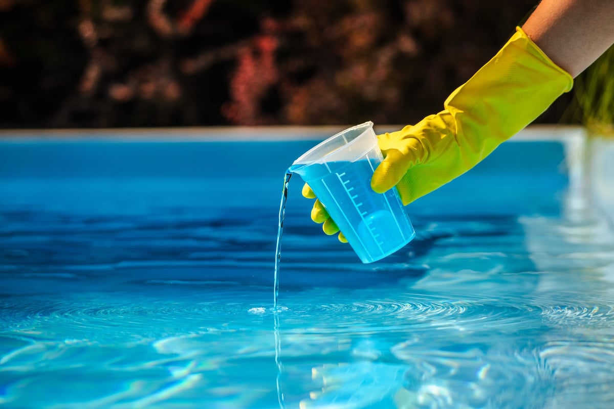 Gloved hand measuring pool chemicals before treating the water