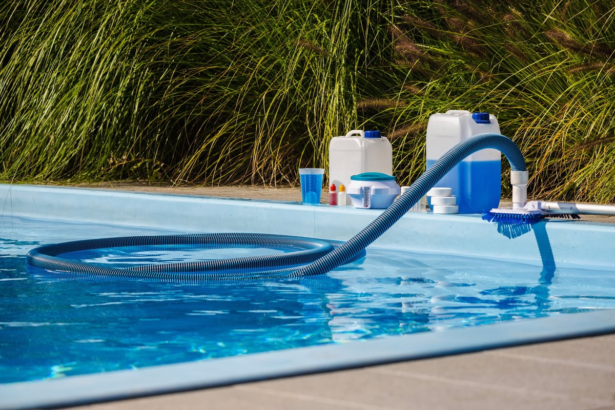 Pool vacuum hose, brush and water testing supplies beside a pool